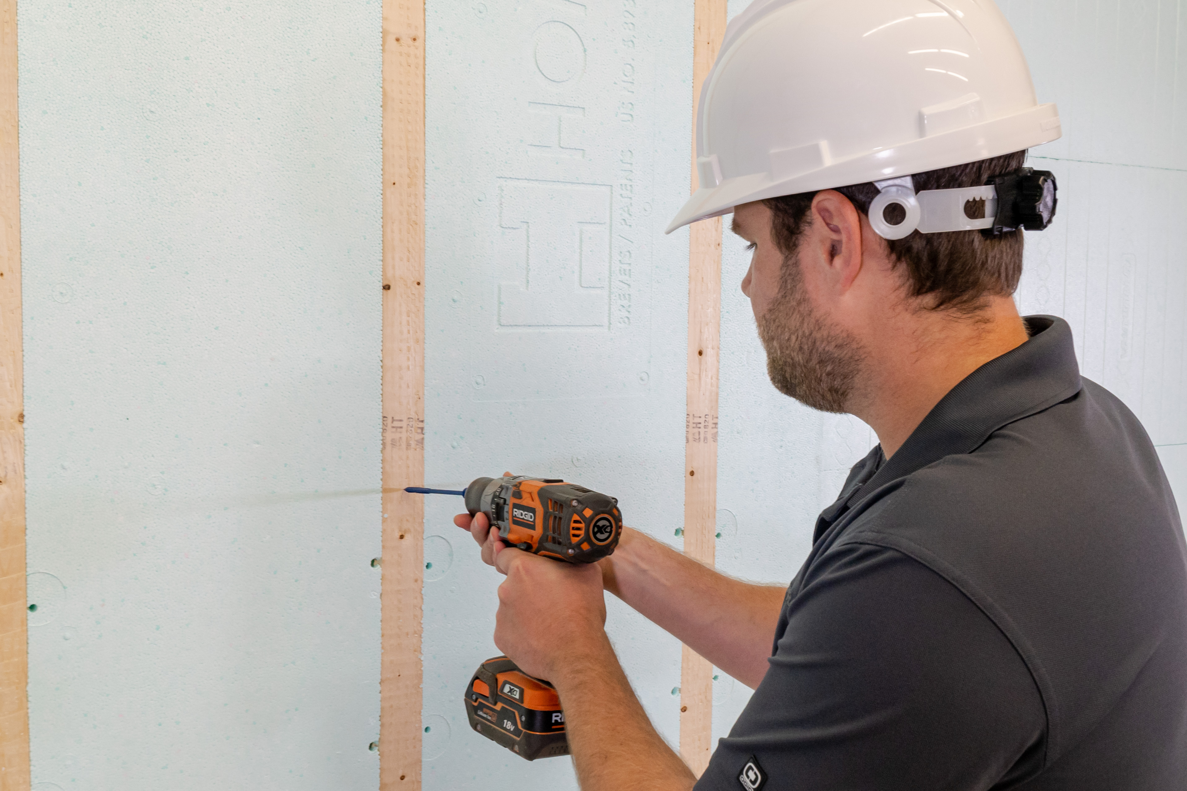 a man wearing a hard hat drills into a wall